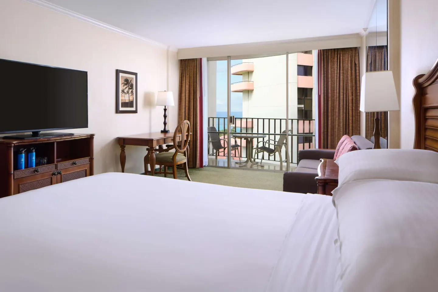 Guest room with king bed at Outrigger Waikiki Beach Resort overlooking a balcony and neighboring tower.