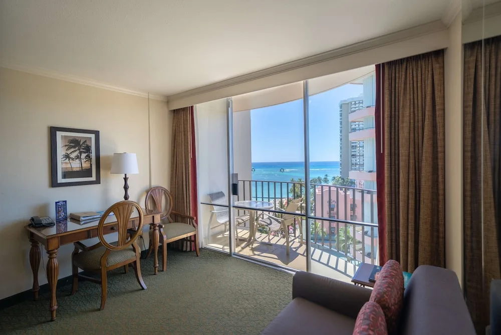 Guest room sitting area at Outrigger Waikiki Beach Resort with desk, balcony, and partial ocean view.