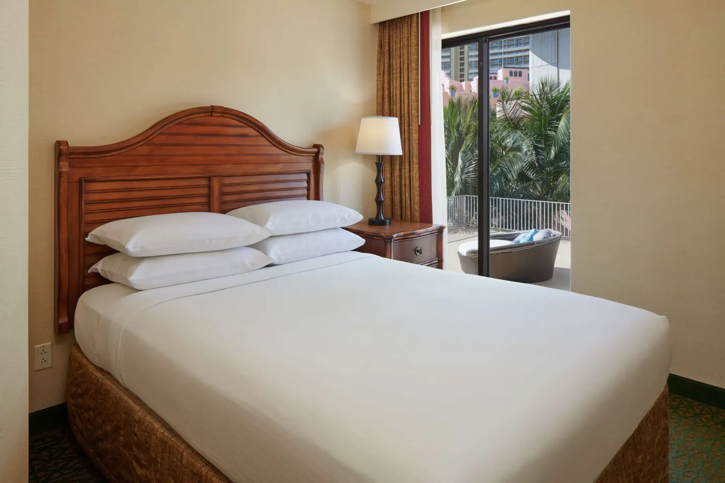 Guest room queen bed beside a lanai with palms at Outrigger Waikiki Beach Resort.