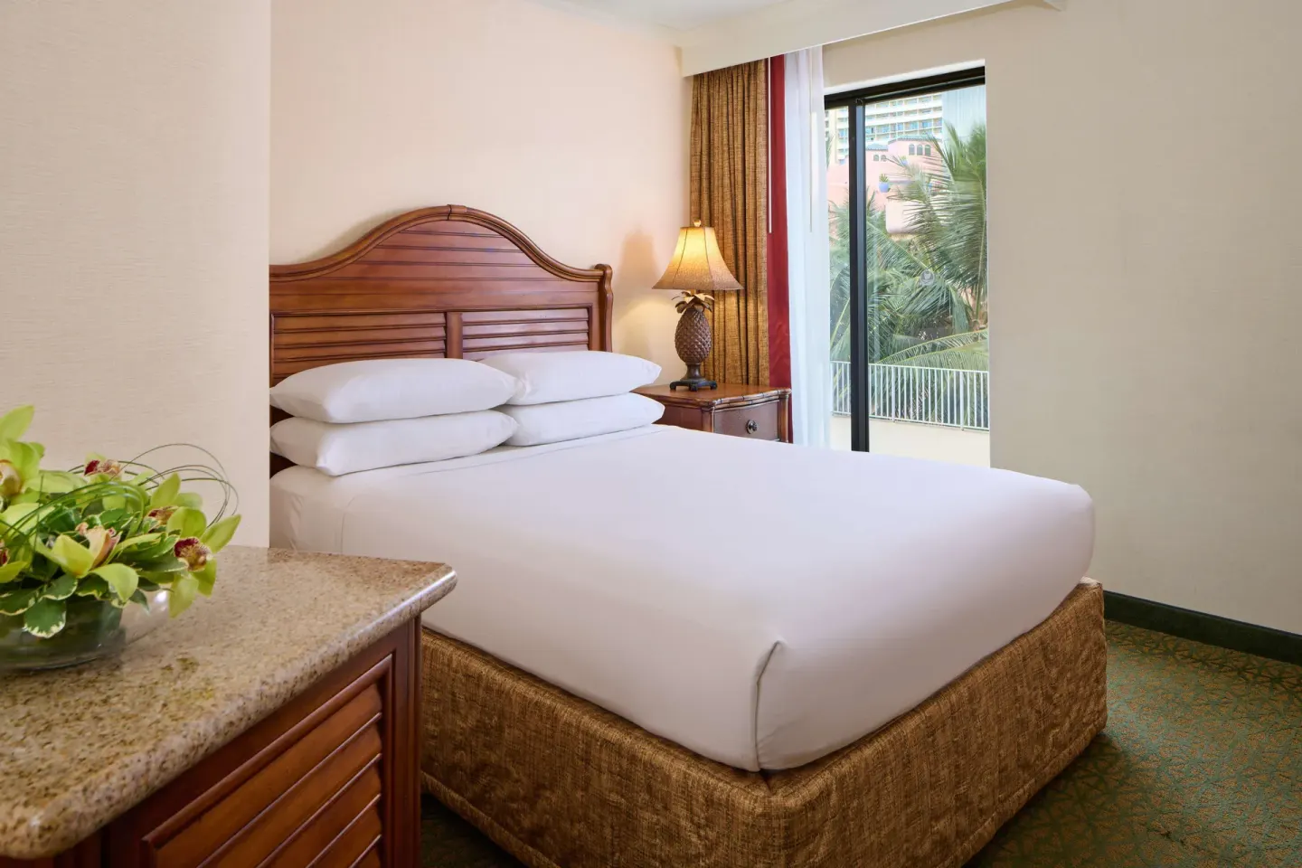 Guest room queen bed with lanai and tropical greenery at Outrigger Waikiki Beach Resort.