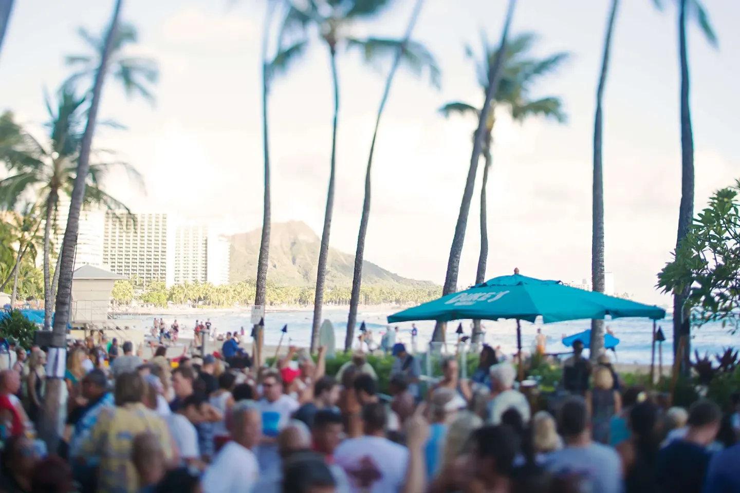 A crowded beachfront patio with palms and Diamond Head at Outrigger Waikiki Beach Resort.