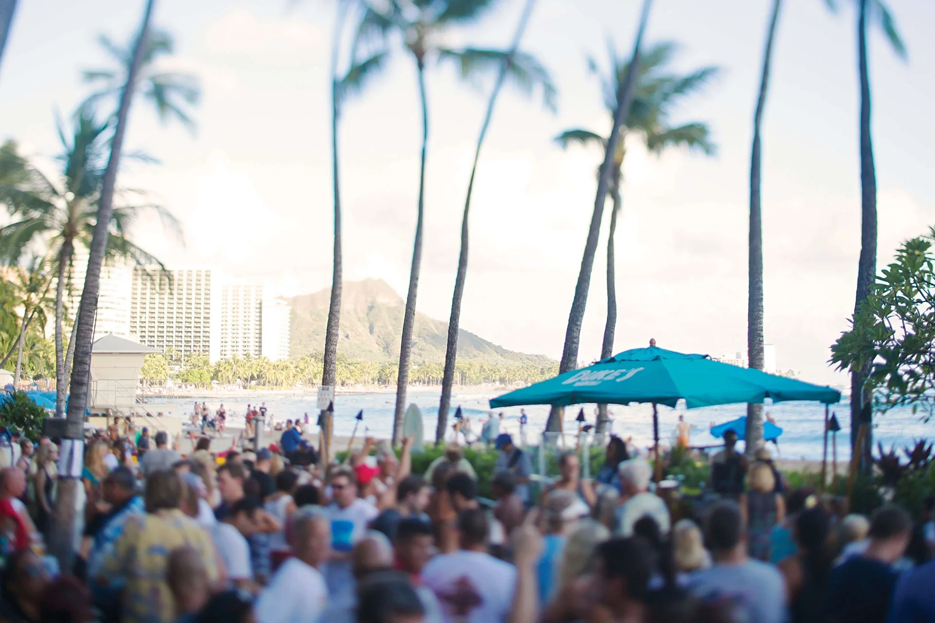 A crowded beachfront patio with palms and Diamond Head at Outrigger Waikiki Beach Resort.