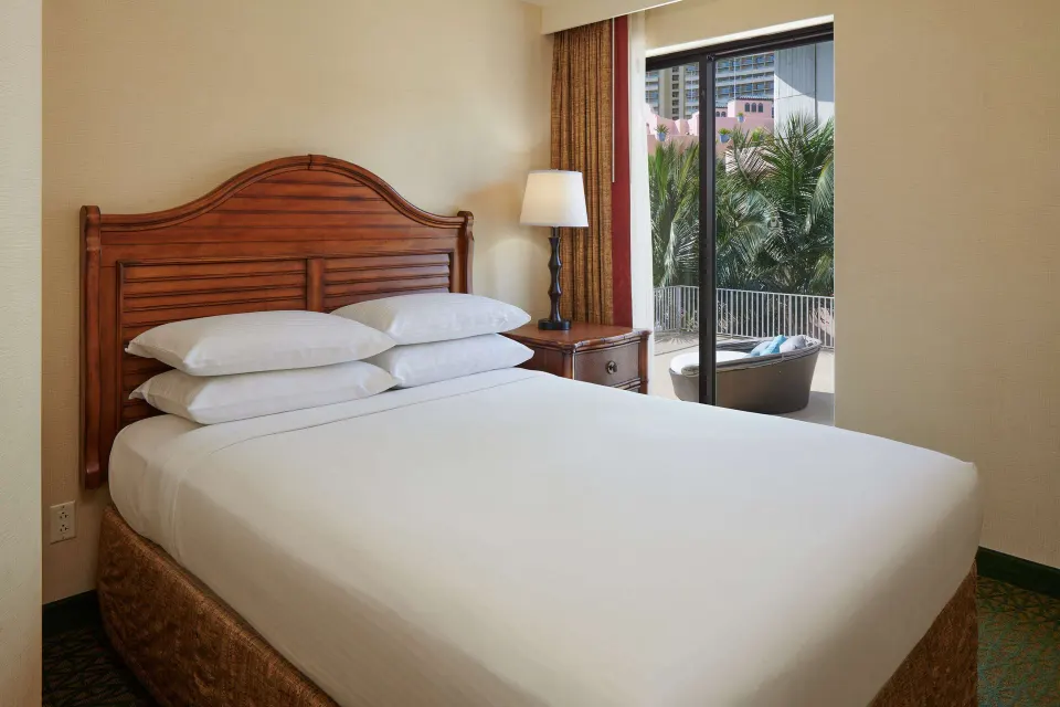 Bedroom with wood headboard and lanai access in a club suite at Outrigger Waikiki Beach Resort.