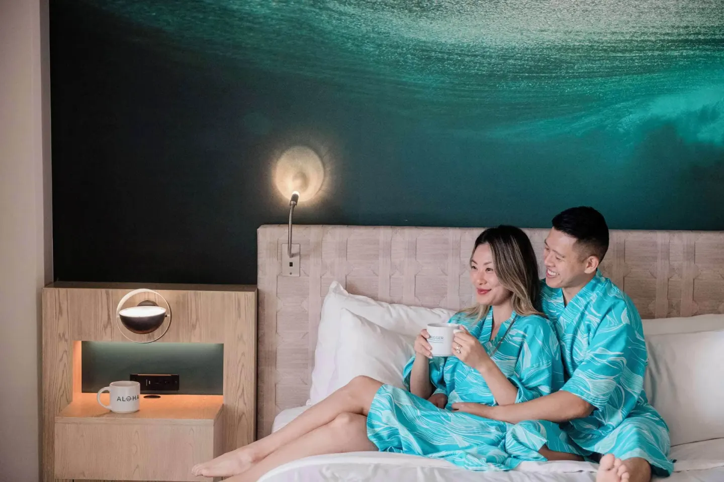 Couple relaxing in bed with mugs at OUTRIGGER Waikiki Beachcomber Hotel.