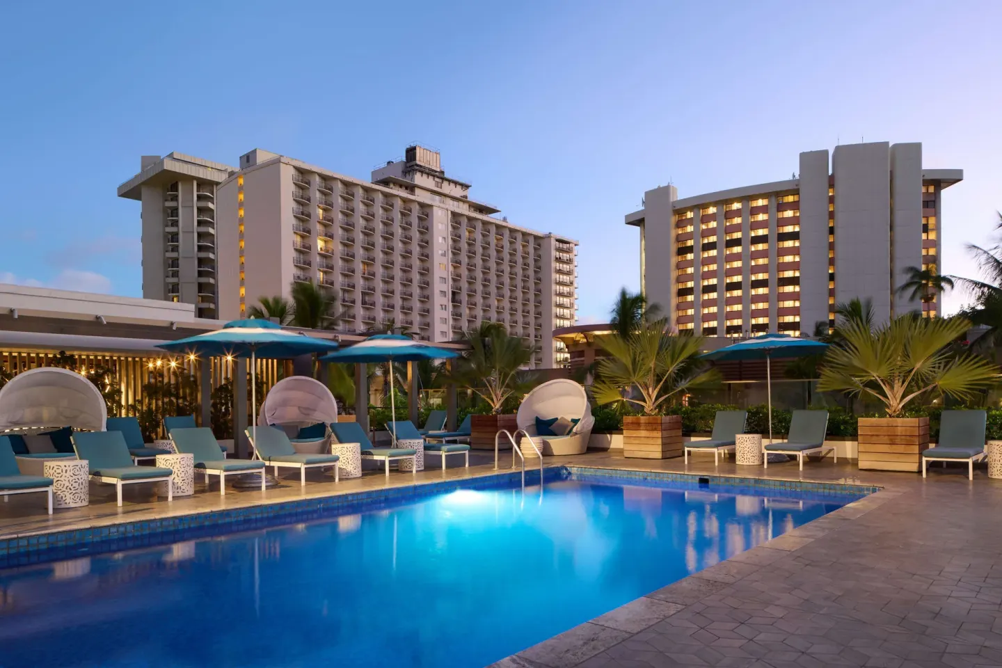 Twilight pool deck with cabanas and umbrellas at OUTRIGGER Waikiki Beachcomber Hotel.