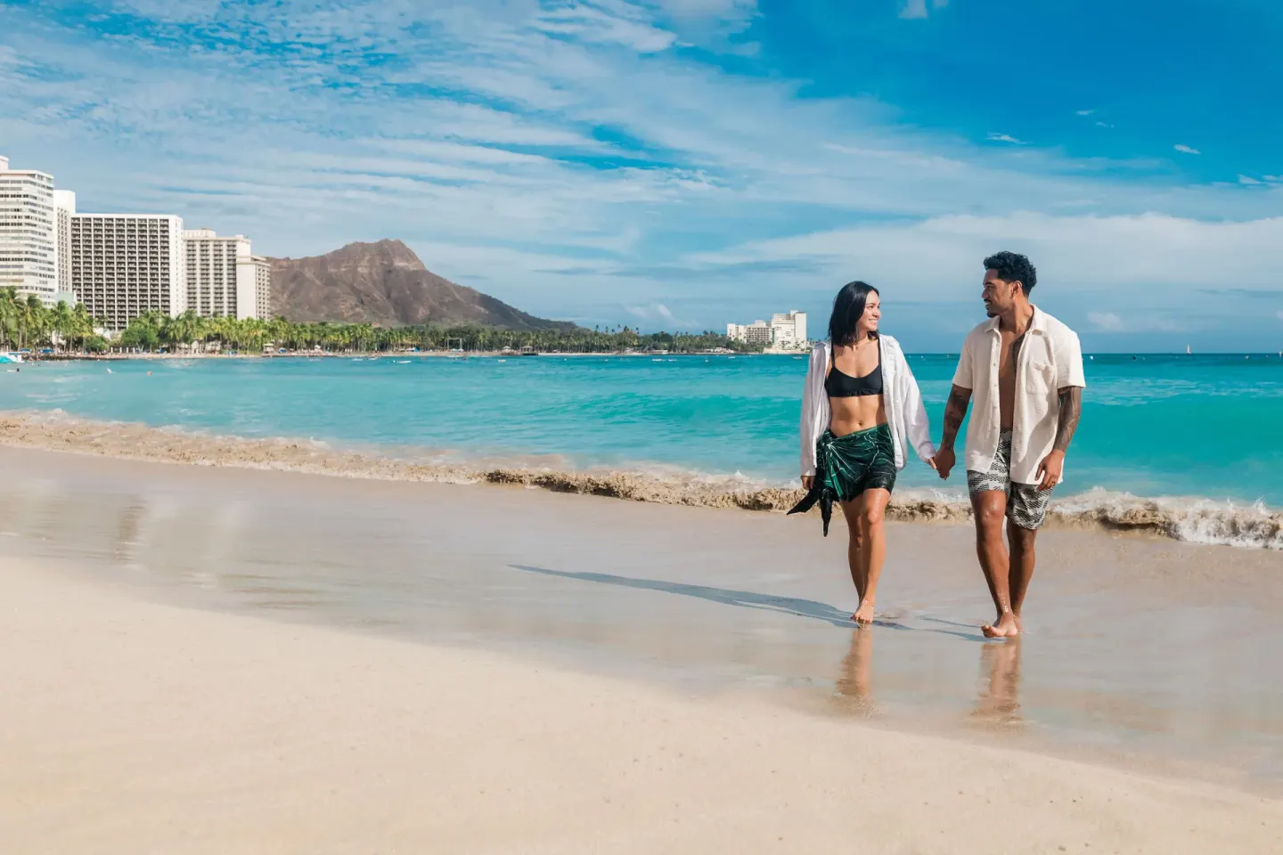 Couple walks on Waikiki Beach near OUTRIGGER Waikiki Beachcomber Hotel.