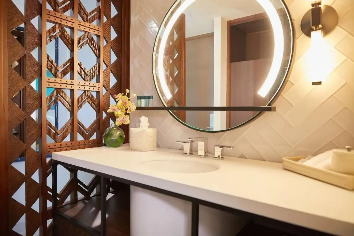 Bathroom sink and round lit mirror in a Partial Ocean View room at Outrigger Waikiki Beachcomber Hotel.