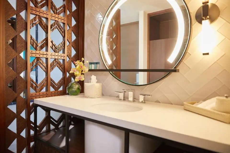 Bathroom sink and round lit mirror in a Partial Ocean View room at Outrigger Waikiki Beachcomber Hotel.