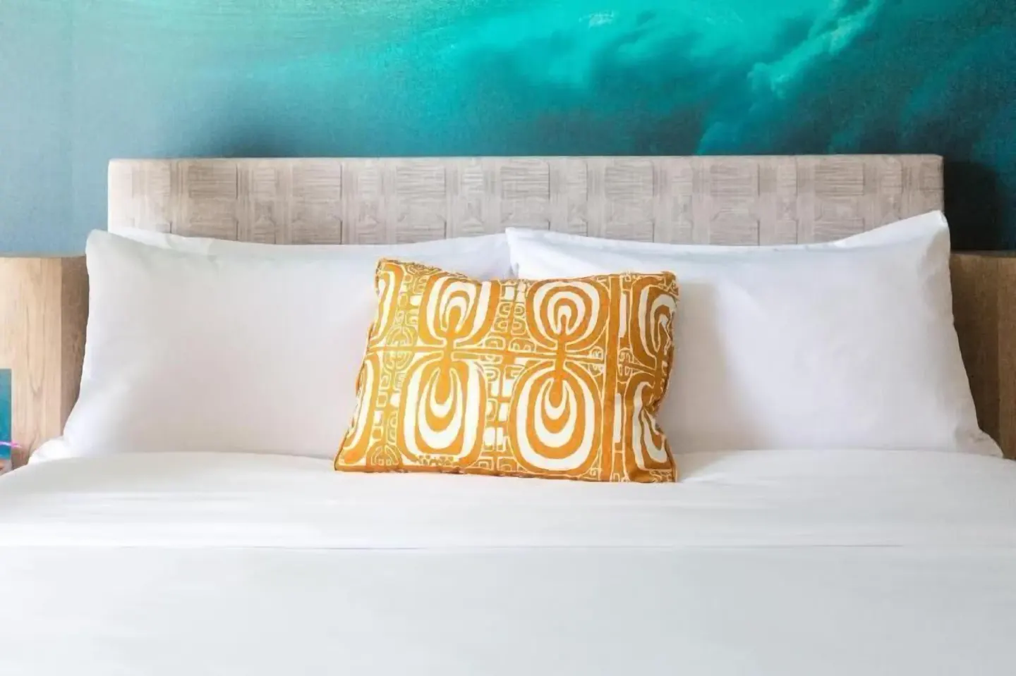 White bed with orange accent pillow in a Partial Ocean View room at Outrigger Waikiki Beachcomber Hotel.