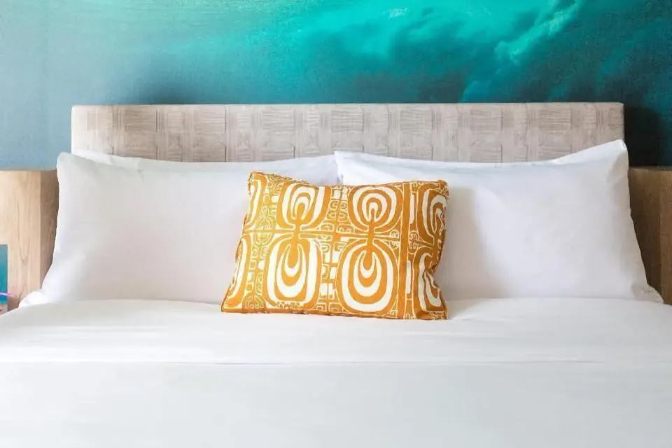 White bed with orange accent pillow in a Partial Ocean View room at Outrigger Waikiki Beachcomber Hotel.