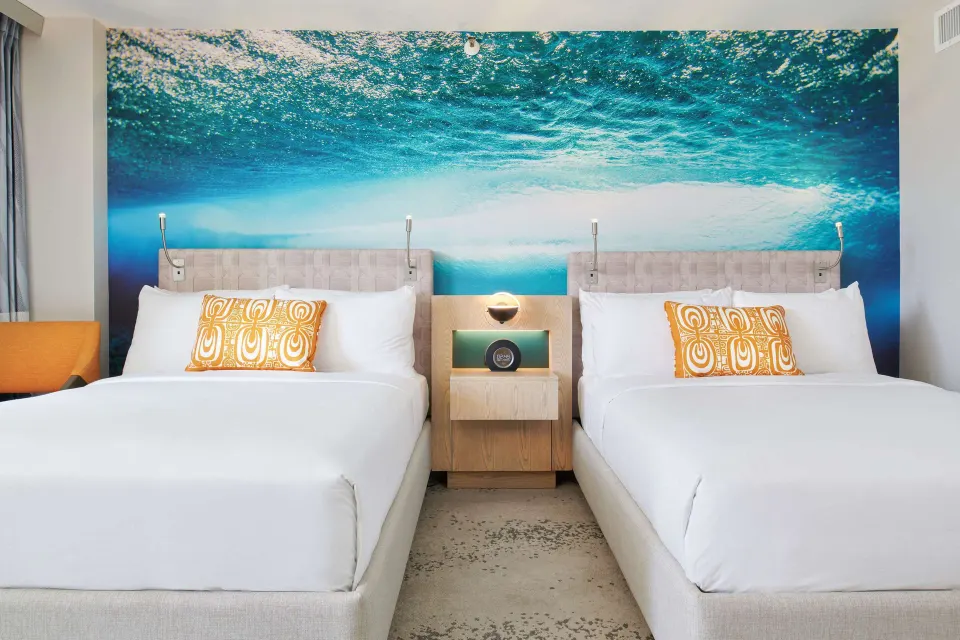 Two queen beds under a wave mural at OUTRIGGER Waikiki Beachcomber Hotel.