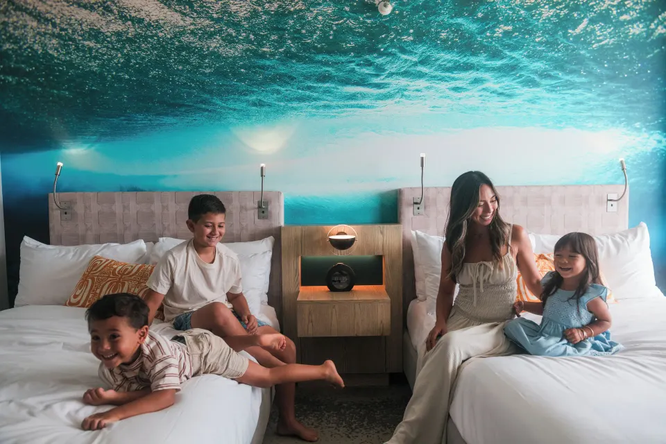 Family relaxing on two queen beds in a Waikiki View room at OUTRIGGER Waikiki Beachcomber Hotel.