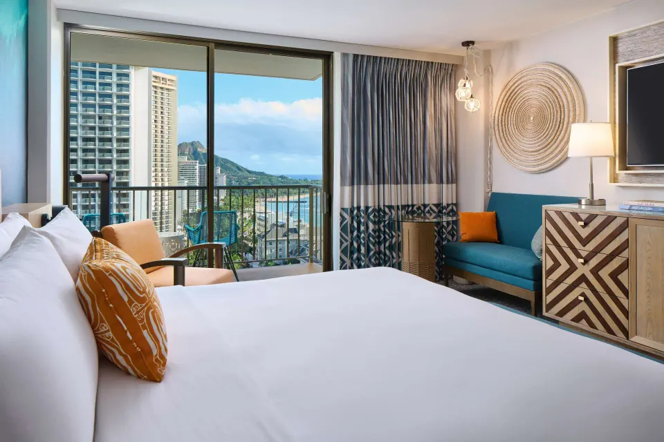 Bedroom with a king bed, sofa, TV, and balcony view at OUTRIGGER Waikiki Beachcomber Hotel.