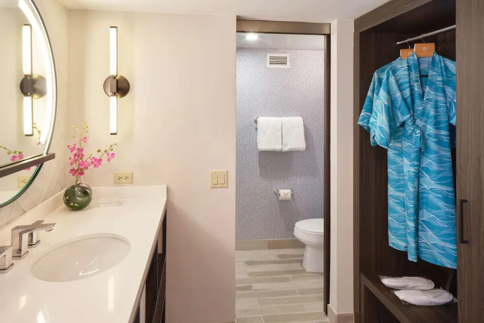 Waikiki View bathroom and closet at OUTRIGGER Waikiki Beachcomber Hotel with vanity, toilet, and robes.