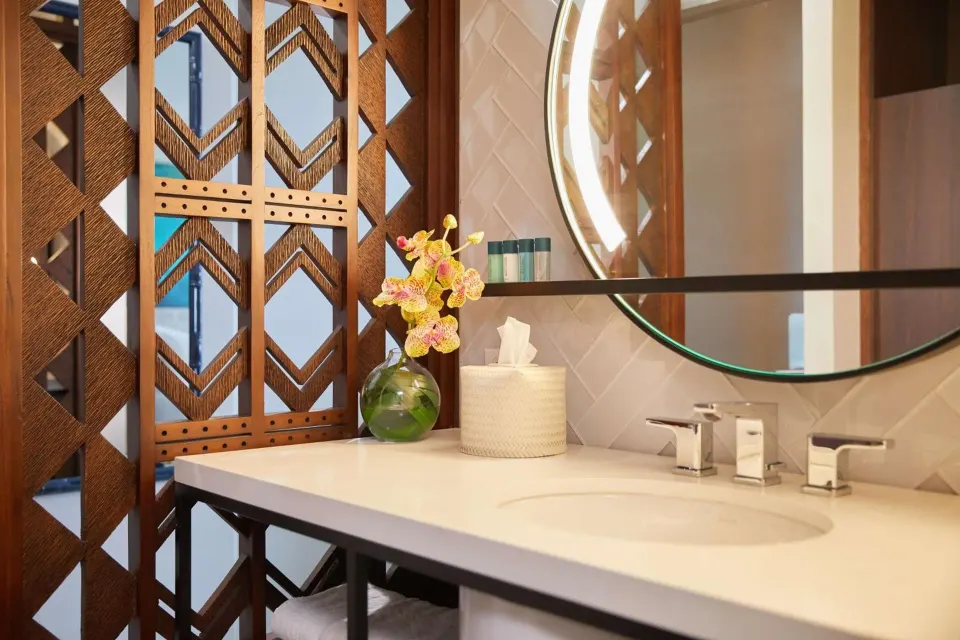 Waikiki View bathroom vanity at OUTRIGGER Waikiki Beachcomber Hotel with round mirror and orchid decor.