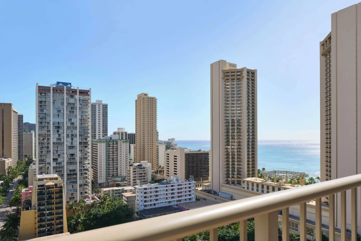 Waikiki skyline and ocean appear beyond a balcony rail at OUTRIGGER Waikiki Paradise Hotel.