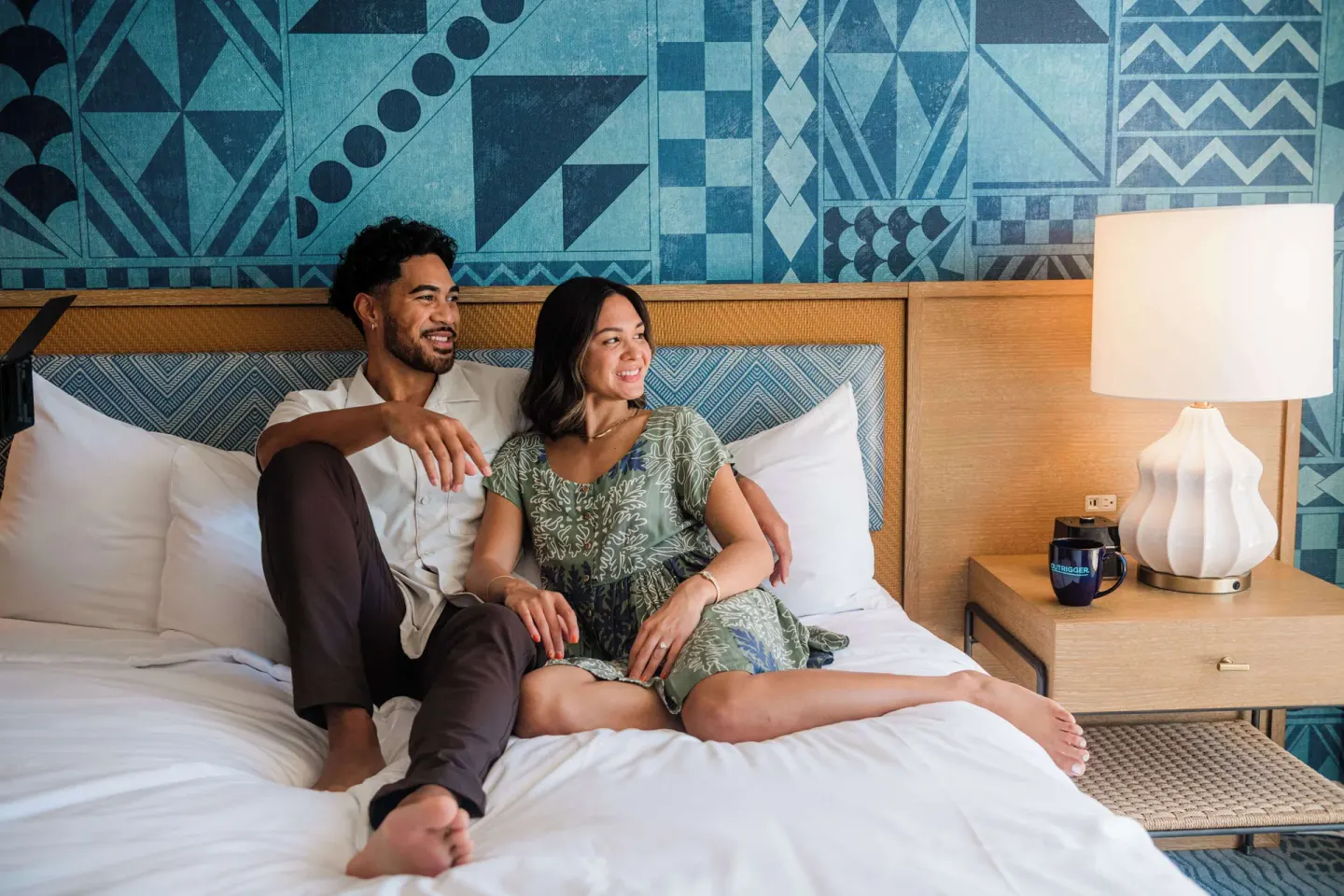 Couple relaxing on a guest room bed at OUTRIGGER Waikiki Paradise Hotel.