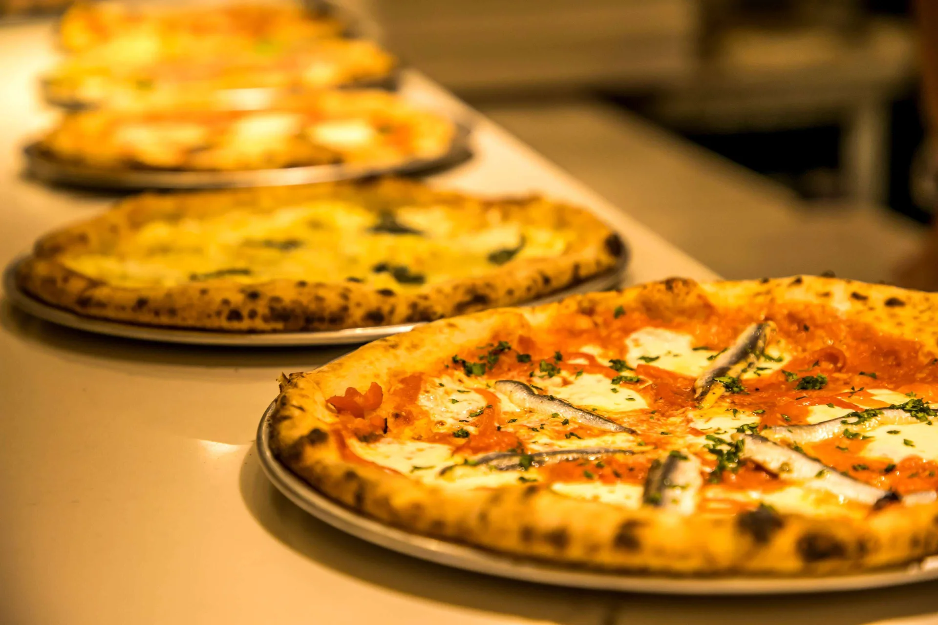 Pizzas sit on metal trays in warm kitchen light at OUTRIGGER Waikiki Paradise Hotel.