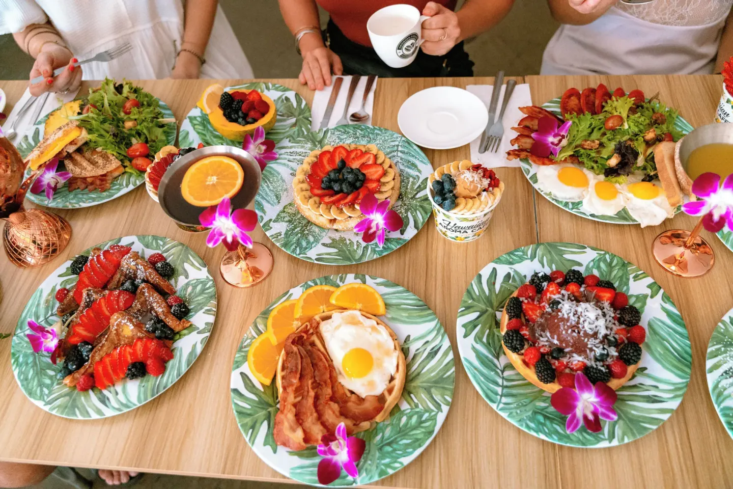 A colorful breakfast table with fruit, eggs, waffles, and drinks at OUTRIGGER Waikiki Paradise Hotel.