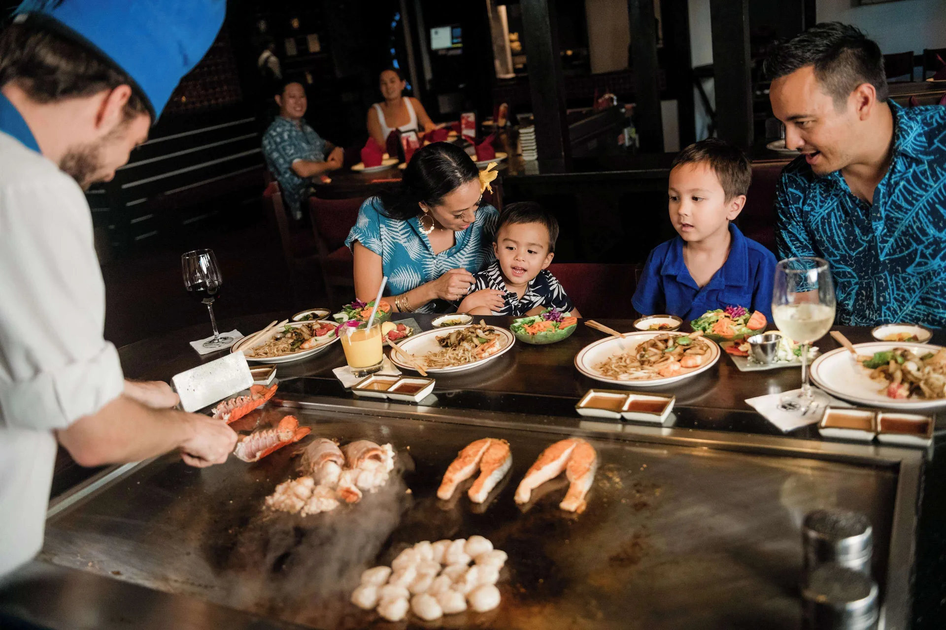 Family watching a teppanyaki chef cook seafood at OUTRIGGER Waikiki Paradise Hotel.