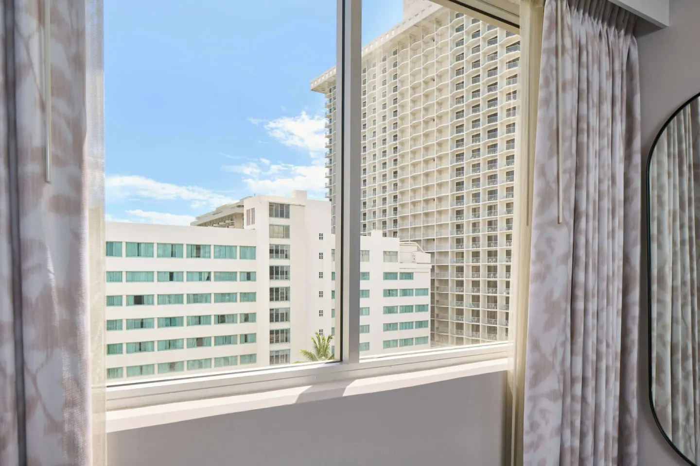 Guest room window with city buildings and curtains at OUTRIGGER Waikiki Paradise Hotel.