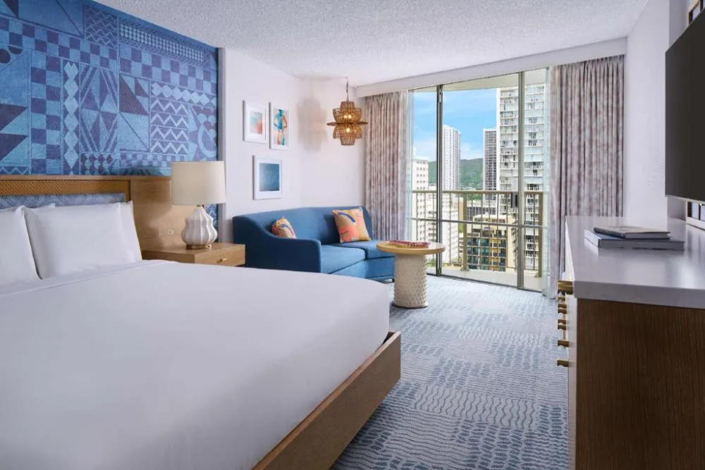 Waikiki View king bed guest room with sofa and city-facing windows at OUTRIGGER Waikiki Paradise Hotel.