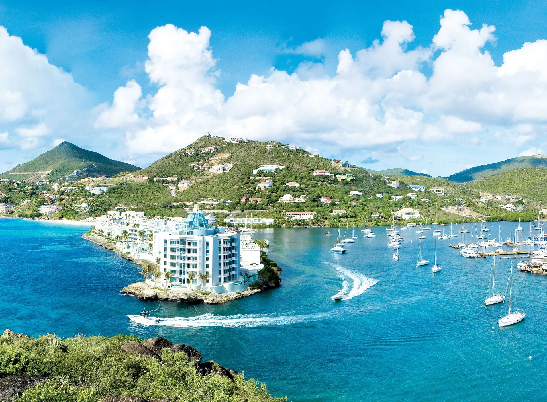 Aerial view of Oyster Bay Beach Resort on a rocky point beside turquoise water and sailboats.