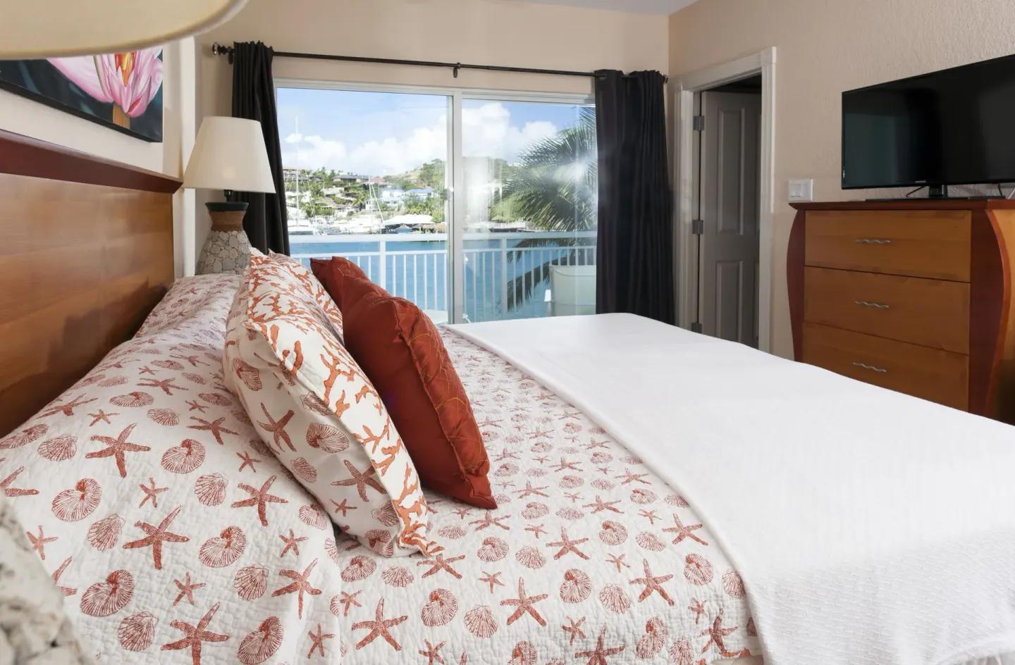Bedroom with shell-pattern bedding and marina-view balcony at Oyster Bay Beach Resort.