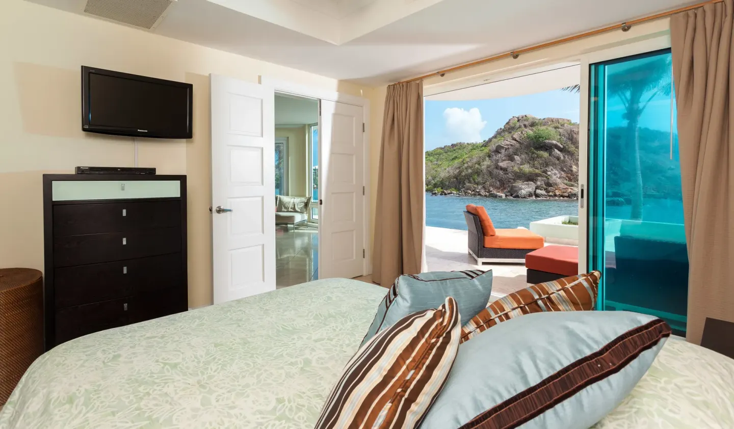 Guest room with bed, TV, and terrace overlooking rocky shoreline at Oyster Bay Beach Resort.