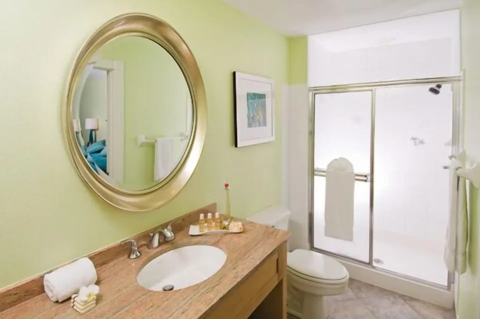 Studio bathroom vanity, round mirror, toilet, and glass shower at Oyster Bay Beach Resort.