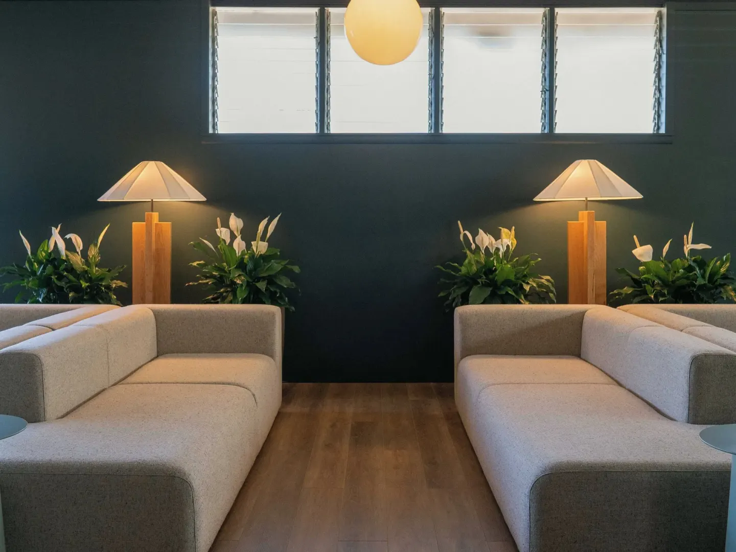 Two facing lobby sofas with lamps, plants, and louvered windows at PACIFIC 19 Kona.