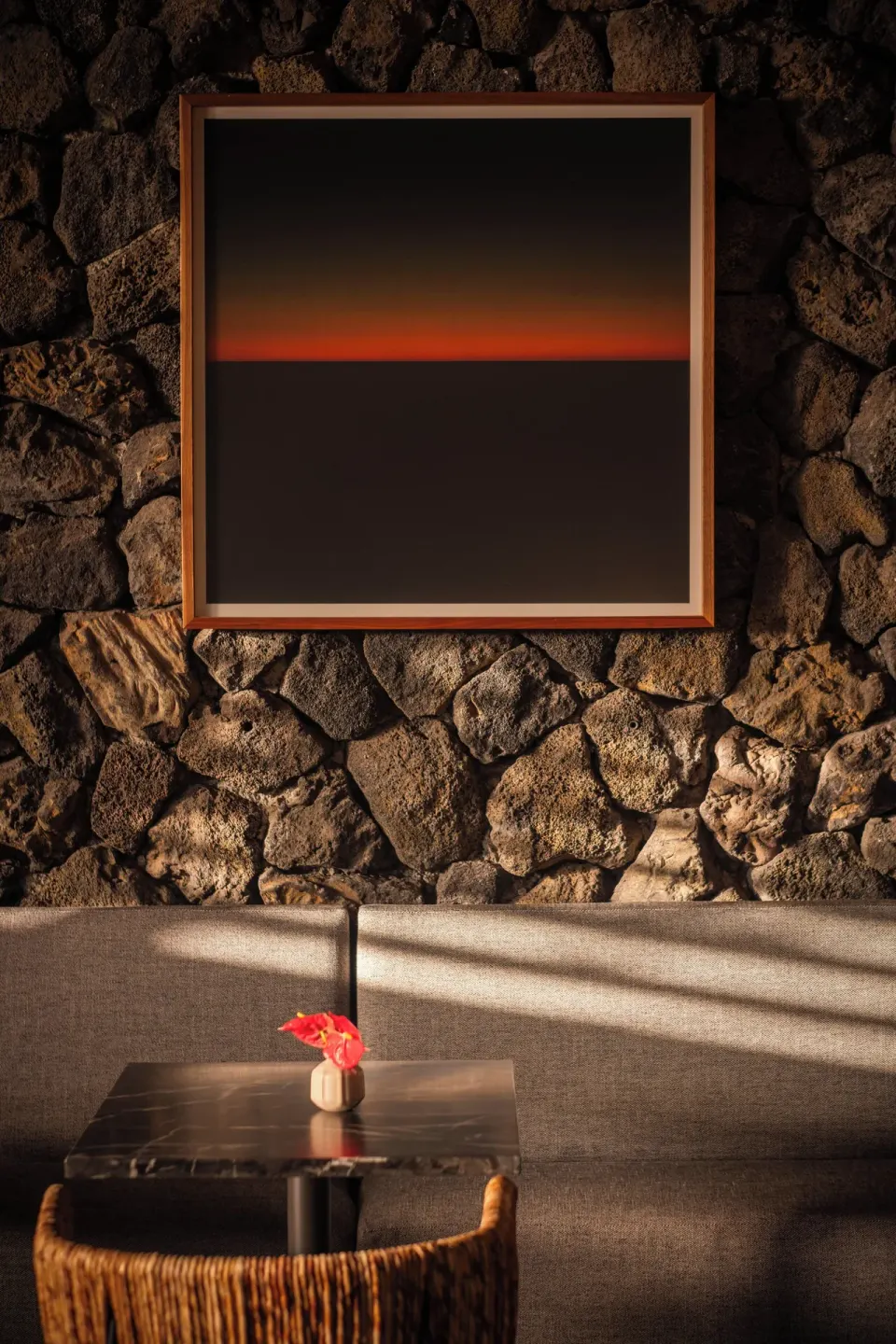 Framed artwork above a bench and table on a stone wall at PACIFIC 19 Kona.