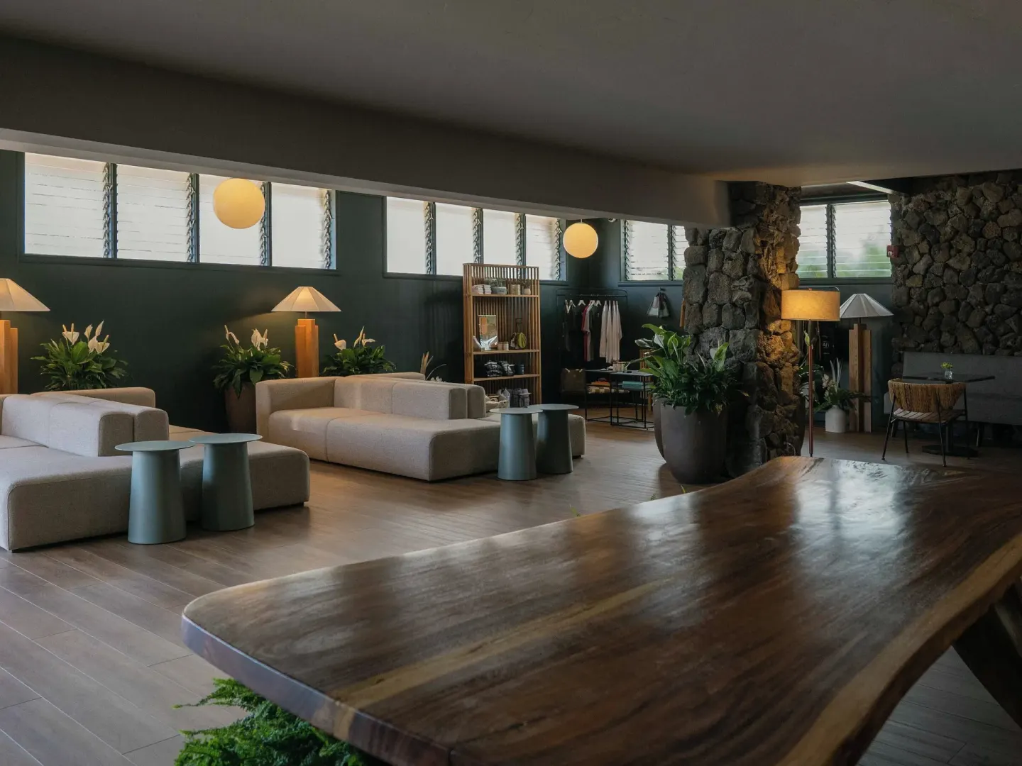 Lobby lounge with a long wood table, sofas, plants, and stone columns at PACIFIC 19 Kona.