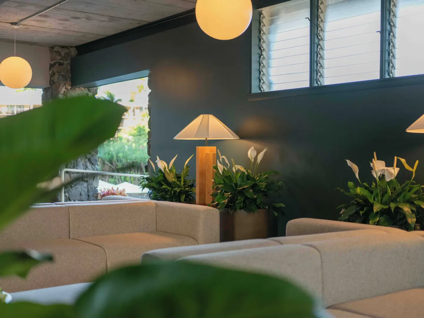 Lobby sofas with plants, lamps, and louvered windows at PACIFIC 19 Kona.