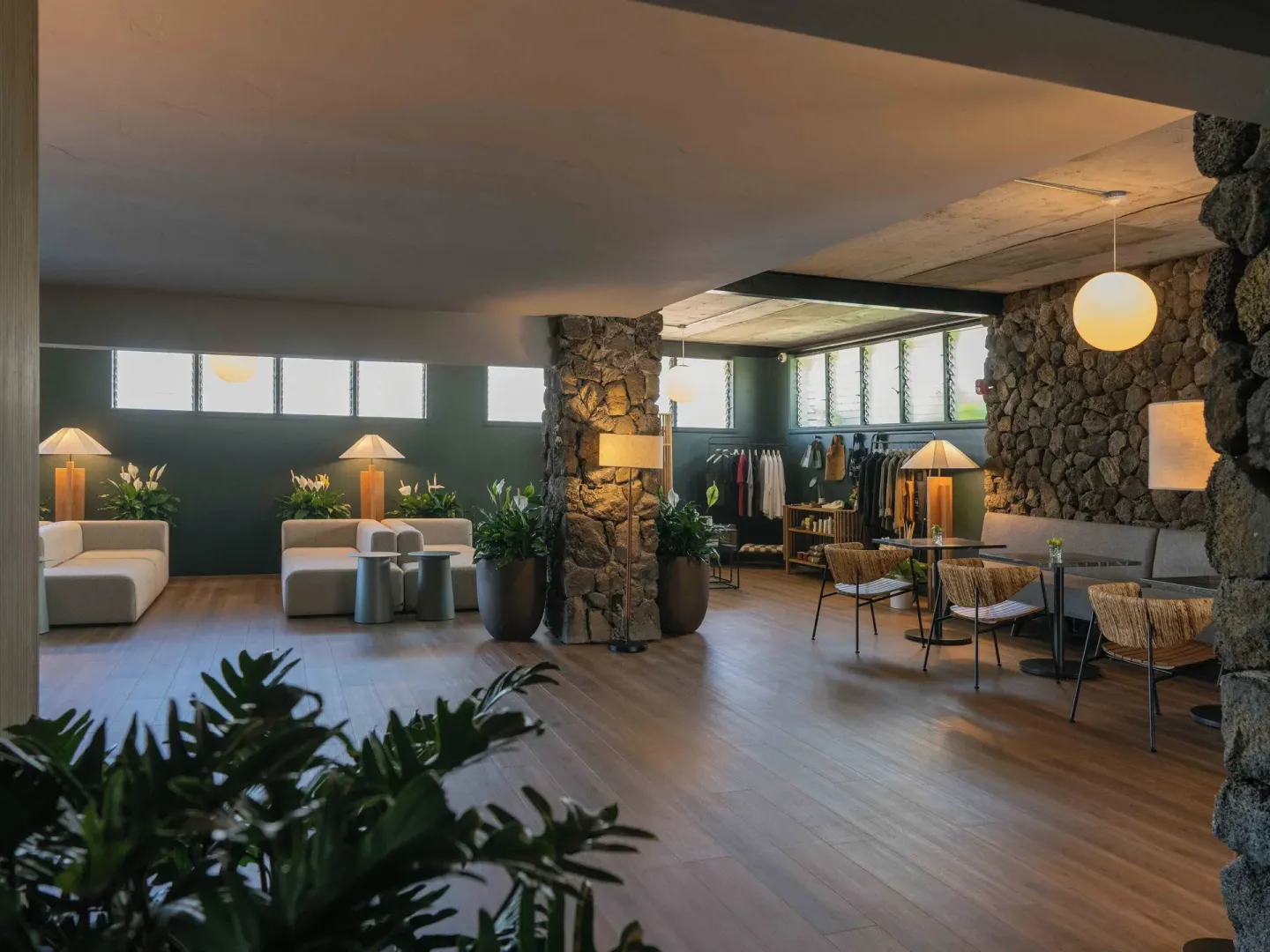 Lobby with stone columns, lounge seating, plants, and café-style tables at PACIFIC 19 Kona.