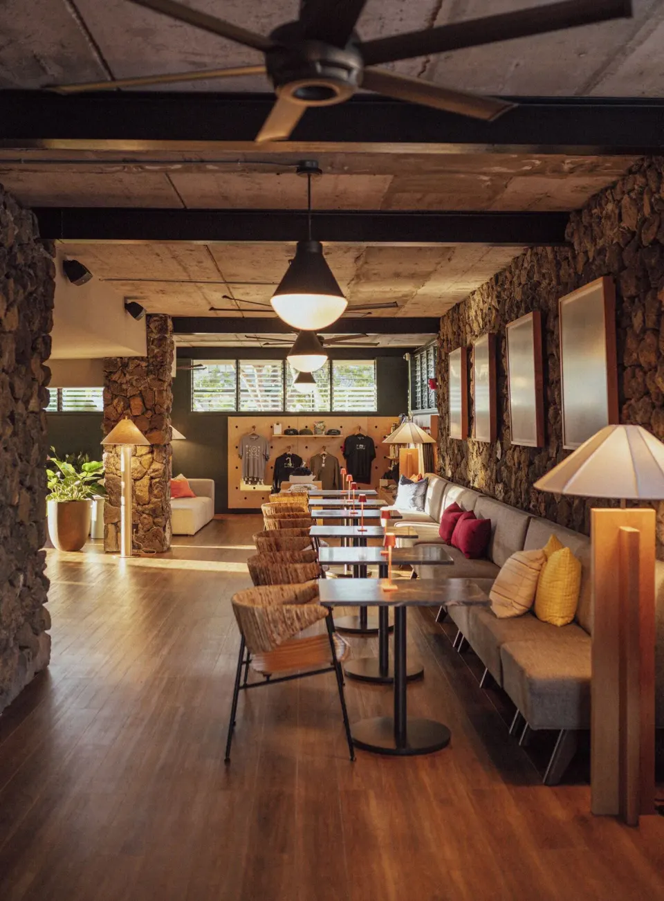 Long lobby lounge with bench seating, tables, fans, and stone walls at PACIFIC 19 Kona.