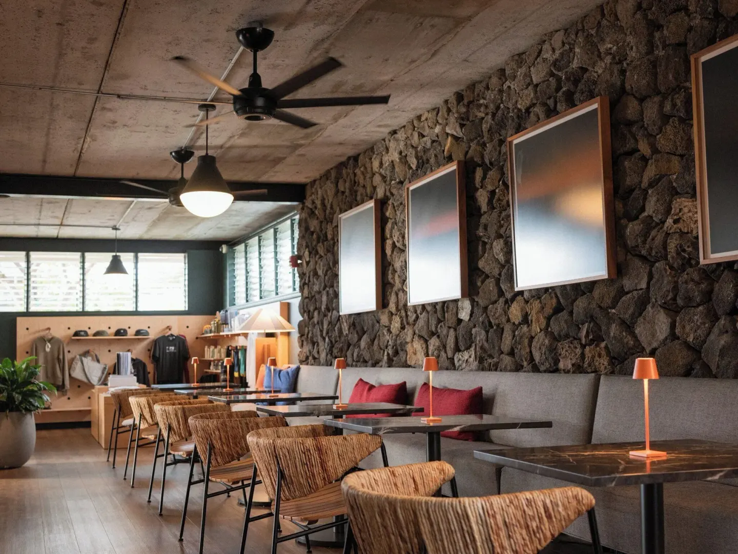 Lounge with woven chairs, stone wall, artwork, and small tables at PACIFIC 19 Kona.