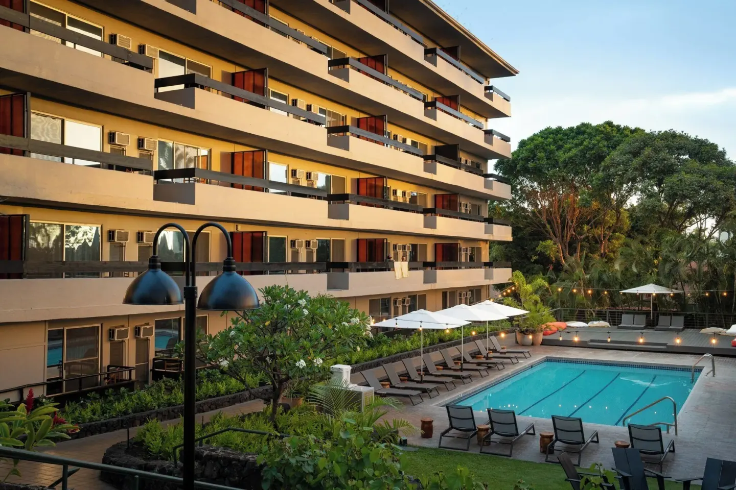 Pool deck with umbrellas, loungers, greenery, and hotel balconies at PACIFIC 19 Kona.