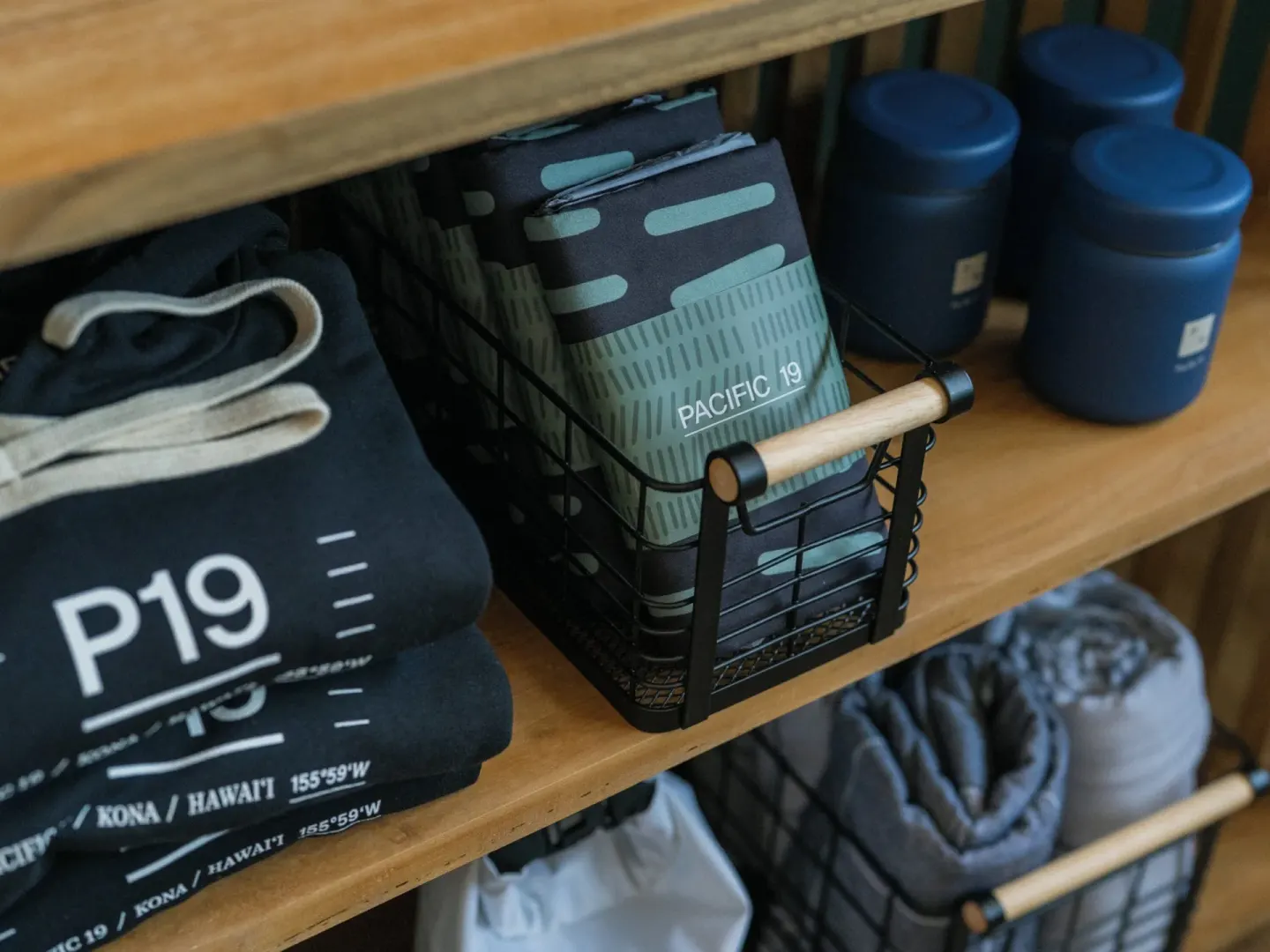 Retail shelves with folded apparel, towels, and blue containers at PACIFIC 19 Kona.