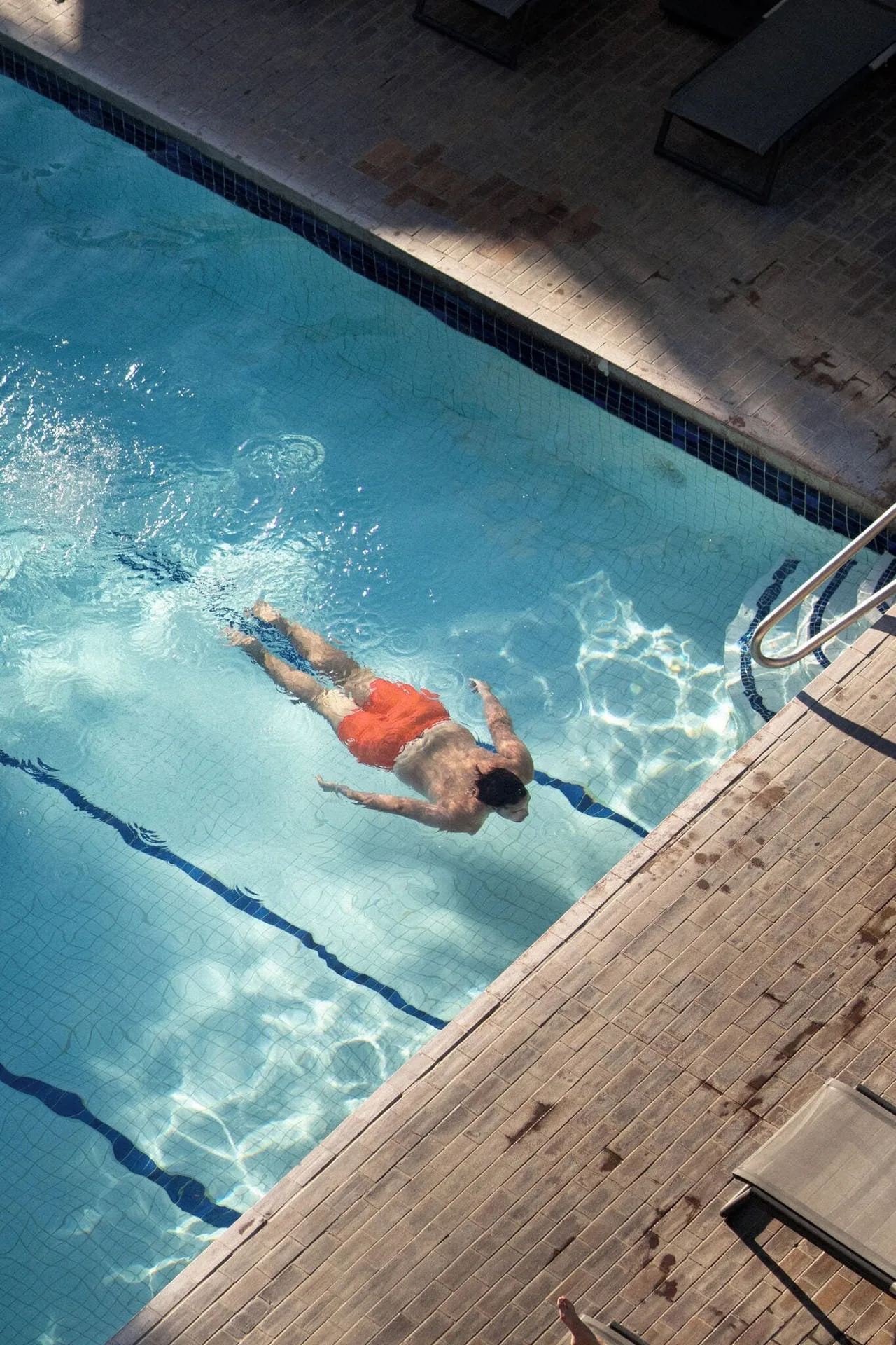 Swimmer in the blue pool near the ladder and sunlit deck at PACIFIC 19 Kona.