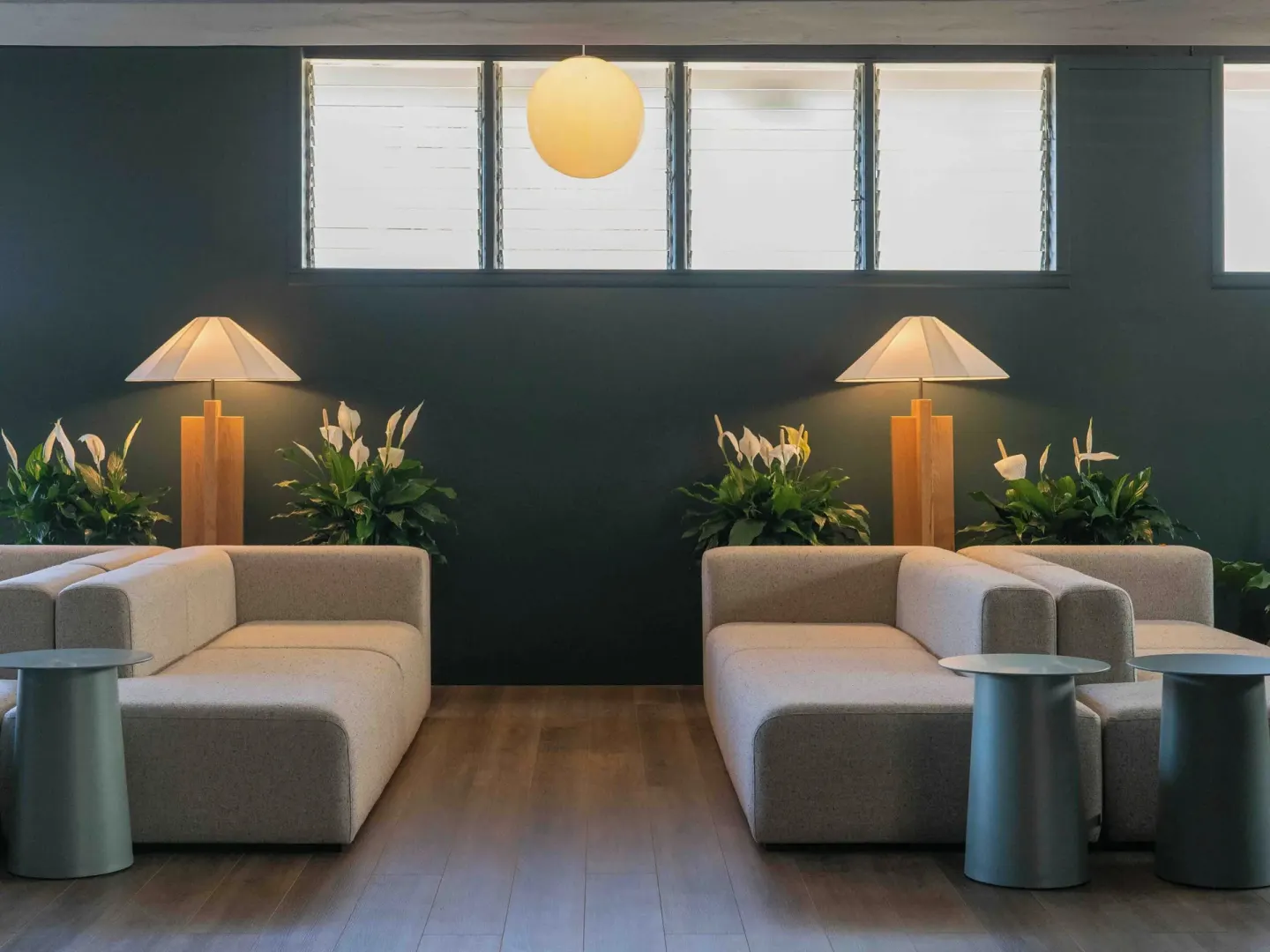 Symmetrical lobby seating with sofas, round tables, lamps, and plants at PACIFIC 19 Kona.