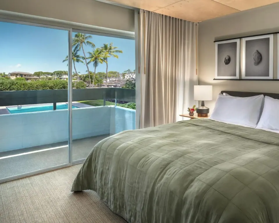 Pool View room king bed beside balcony doors overlooking pool and palms at PACIFIC 19 Kona.