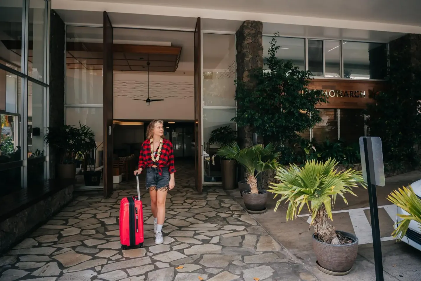 Guest with red suitcase at the entrance to Pacific Monarch Hotel.
