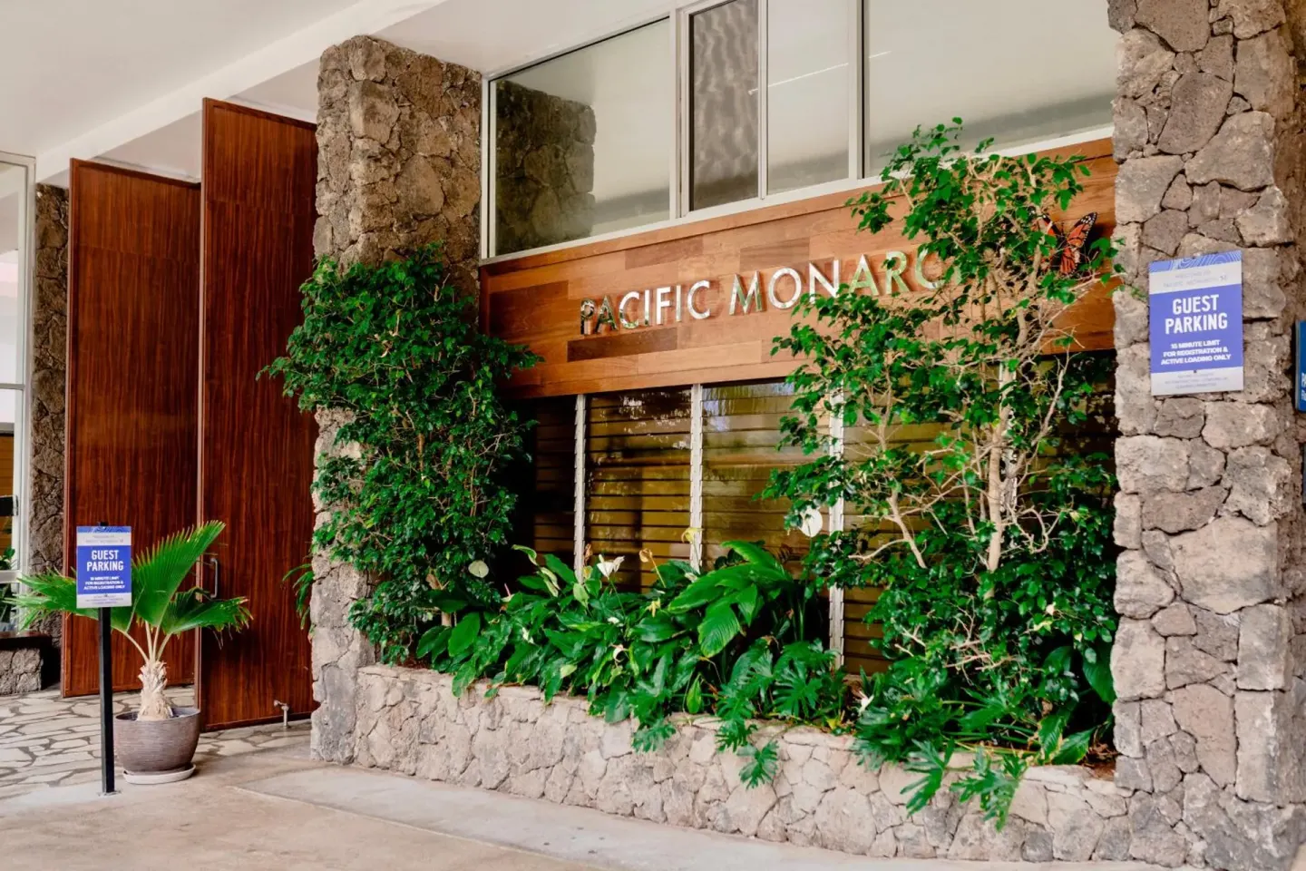 Pacific Monarch Hotel entrance with stone columns, greenery, and guest parking signs.