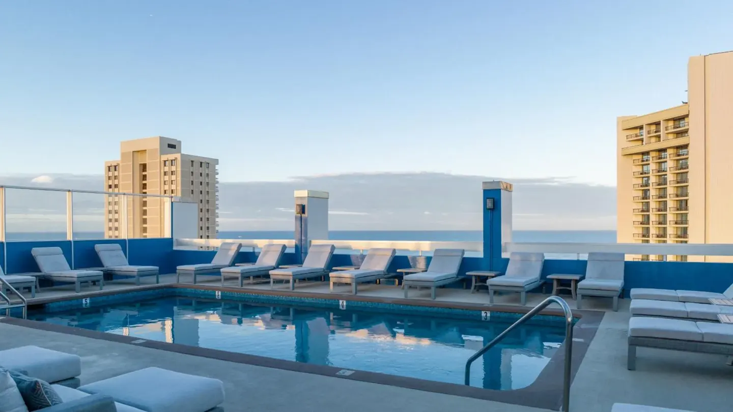 Rooftop pool with lounge chairs and ocean glimpses at Pacific Monarch Hotel.