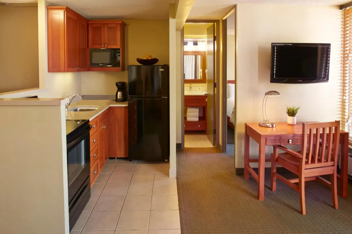 Suite kitchenette, desk, and wall-mounted TV at Pacific Monarch Hotel.