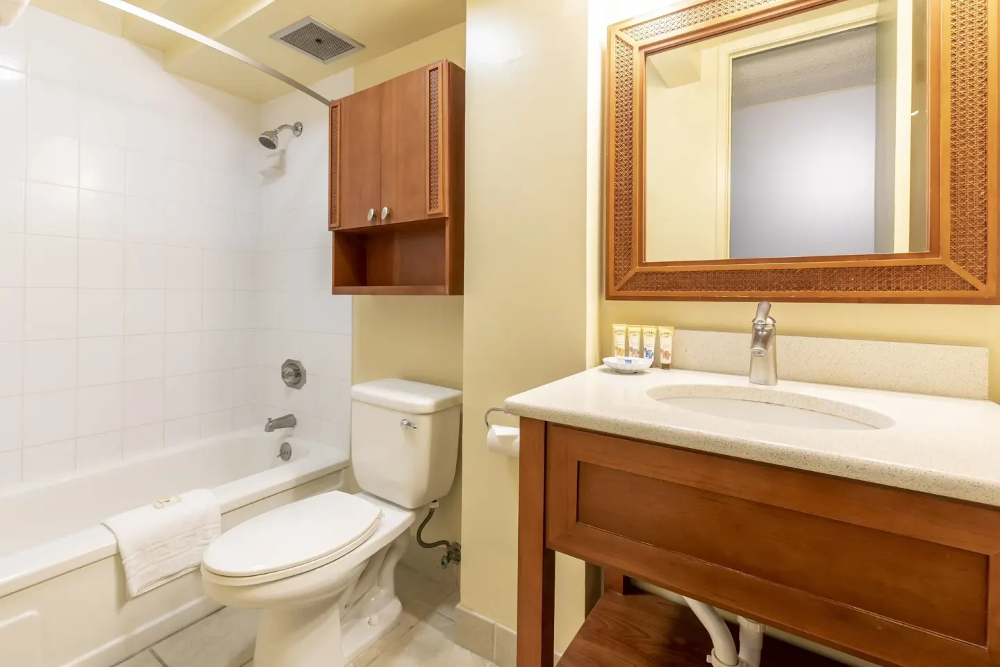 Studio suite bathroom with tub-shower, toilet, vanity, mirror, and amenities at Pacific Monarch Hotel.