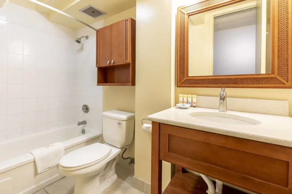Studio suite bathroom with tub-shower, toilet, vanity, mirror, and amenities at Pacific Monarch Hotel.
