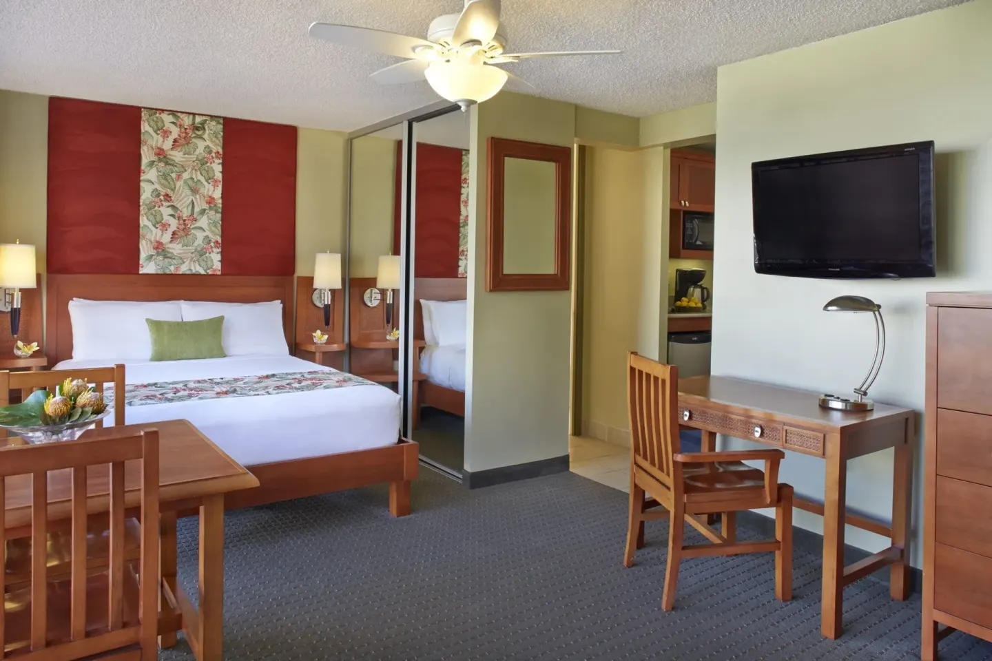 Studio suite with king bed, dining table, desk, TV, and kitchenette doorway at Pacific Monarch Hotel.