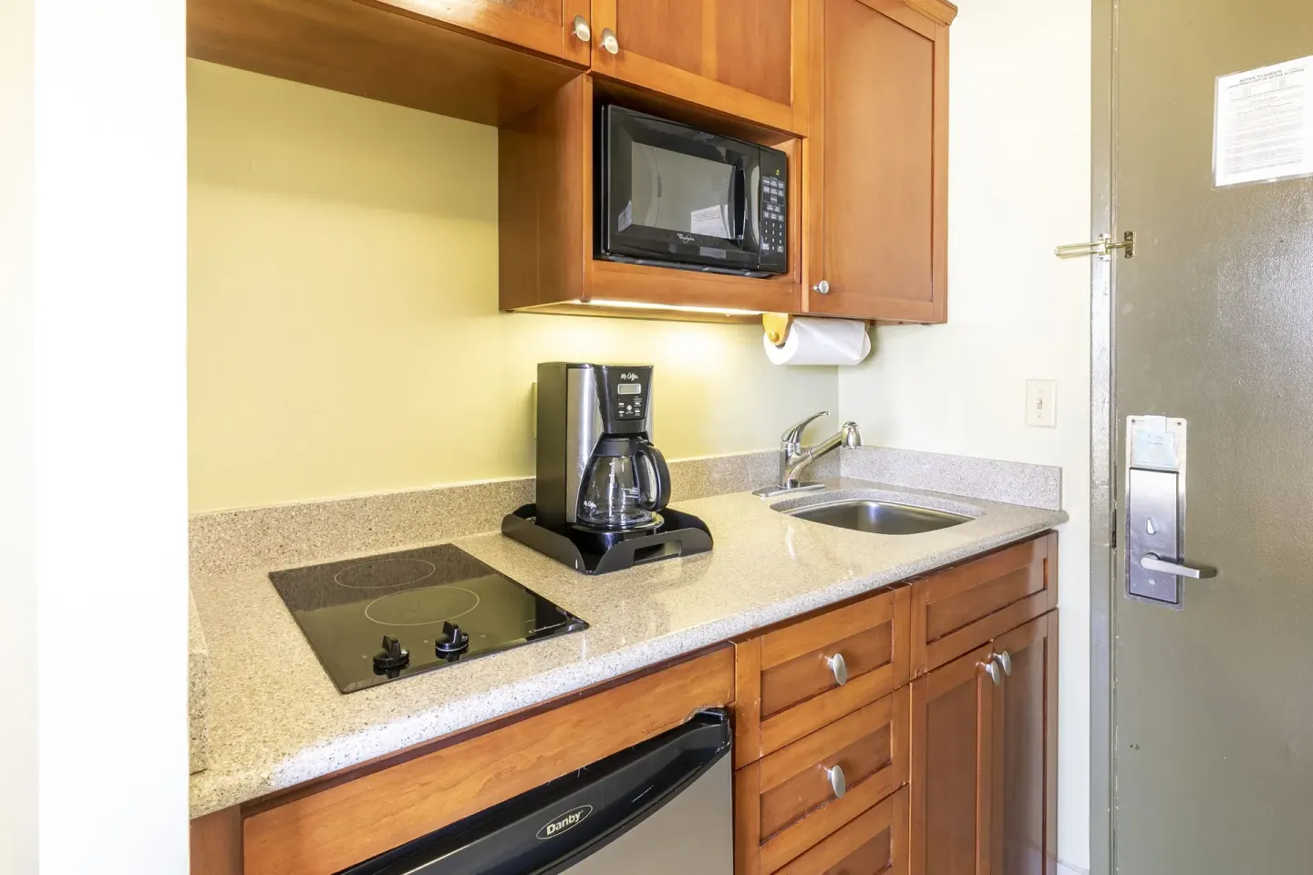 Studio Suite kitchenette with cooktop, coffee maker, sink, microwave, and cabinets at Pacific Monarch Hotel.